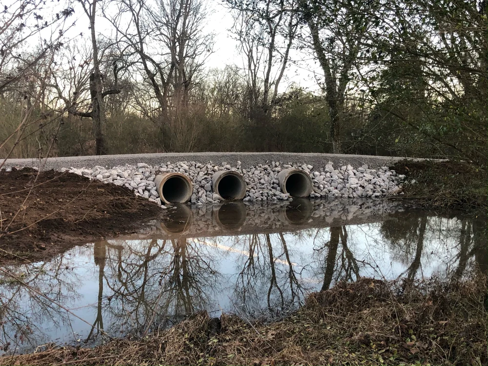 A triple culvert crossing set in riprap stone over a creek, with the roadway built across the top
