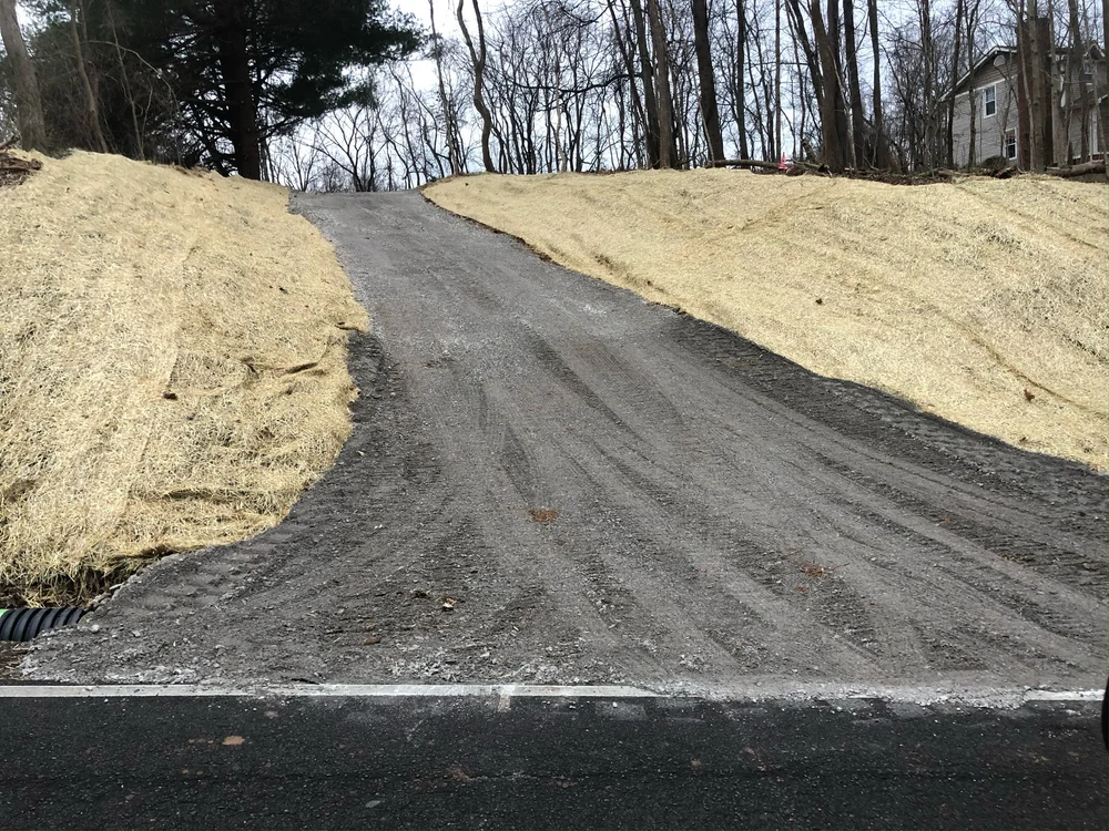 A newly installed gravel driveway with a straw-covered shoulder running through wooded land