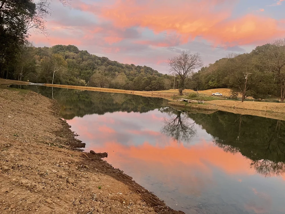 A finished farm pond at sunset with the sky reflected on still water