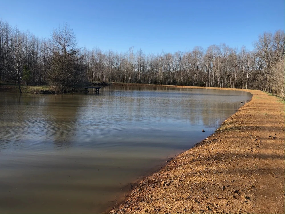 A large completed farm pond filled with water under a clear blue sky